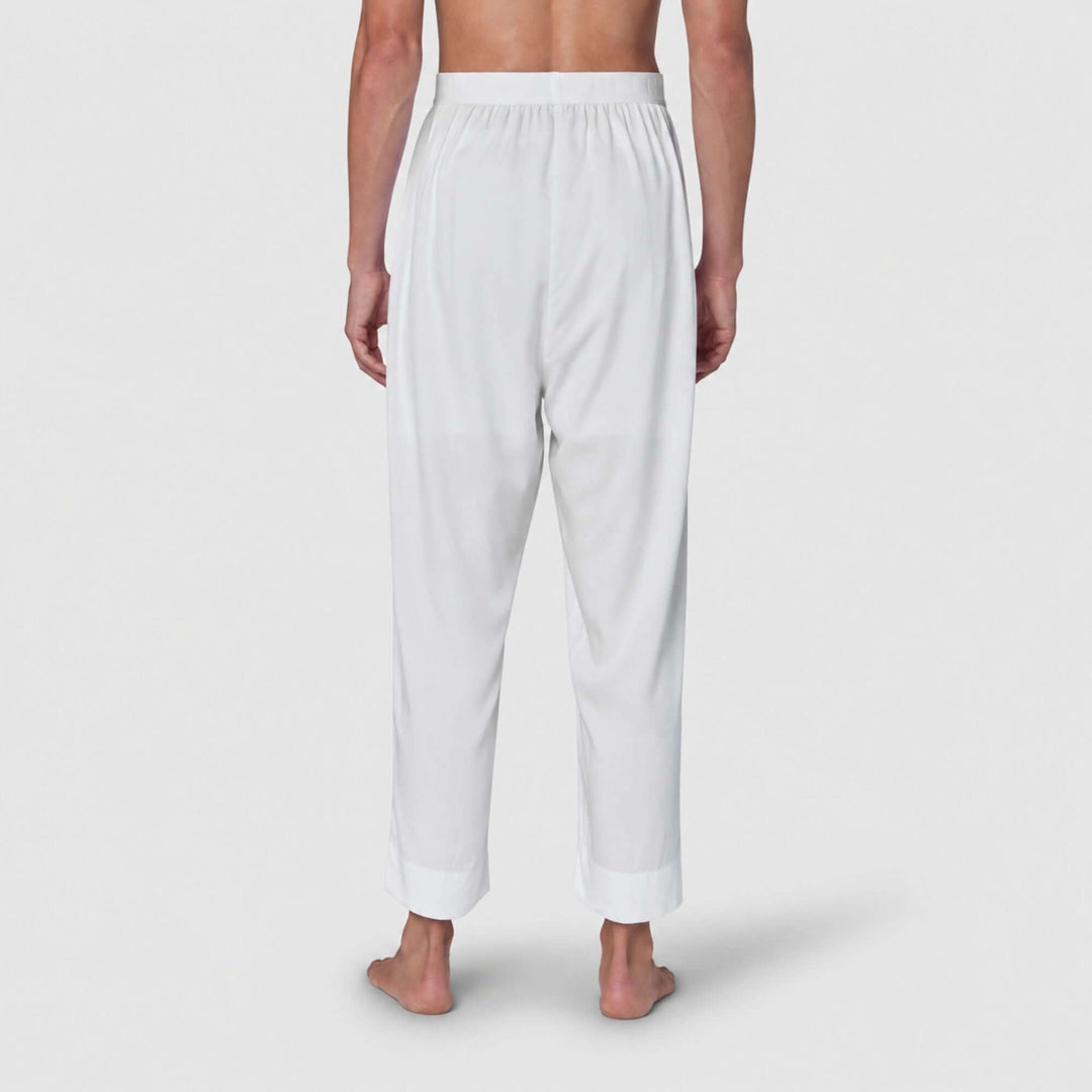 White lounge pants shown from the back on a model, featuring an elastic waistband and relaxed straight-leg fit with rolled cuffs, against a light gray studio background.