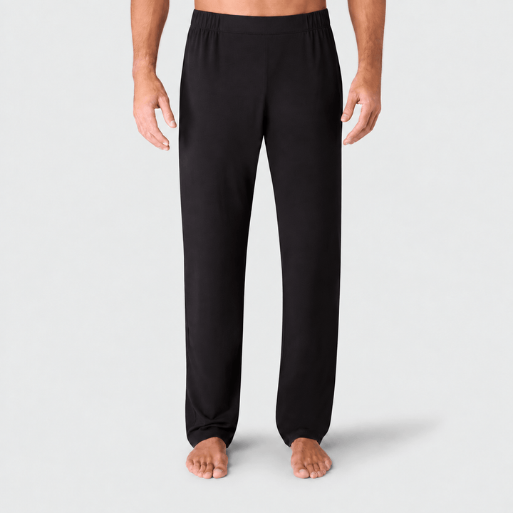 A person wearing black lounge pants, shown from the waist down against a light gray studio background.